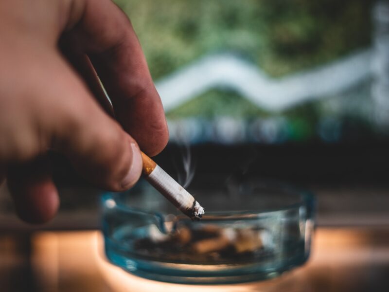 person holding cigarette stick and round glass ashtray