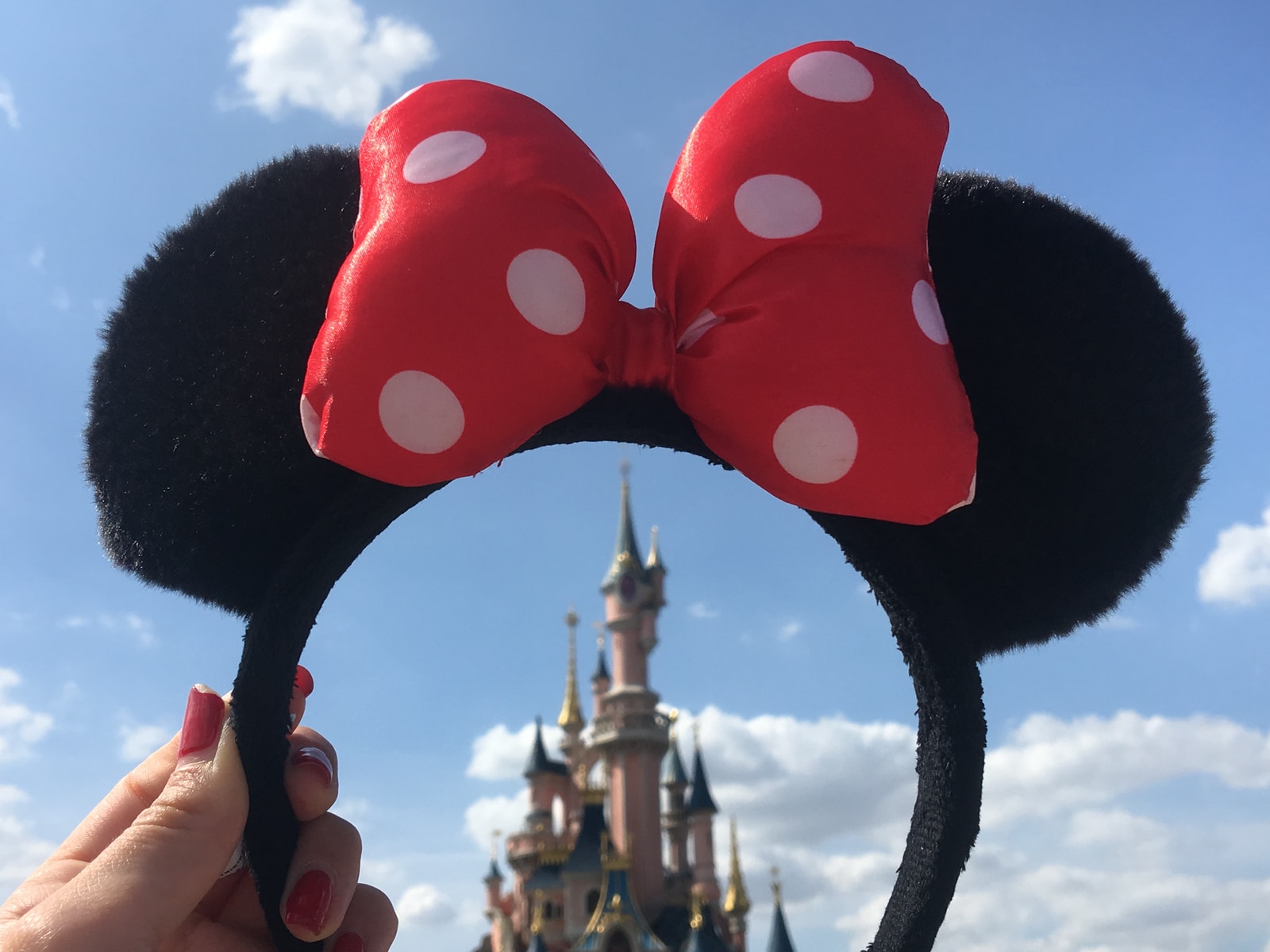 person holding Minnie Mouse headband overlooking castle