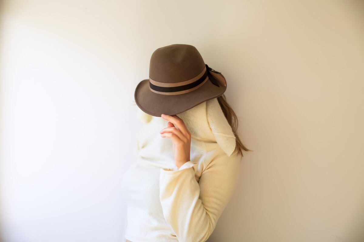 person wearing white crew-neck long-sleeved shirt and brown hat standing and covering face with white towel