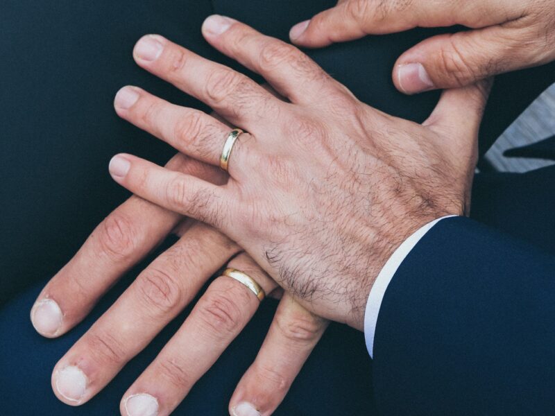 two man's hands wearing gold-colored wedding rings